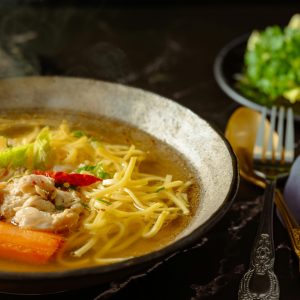 Capture of a flavorful chicken noodle soup with garnishes in a rustic setting.