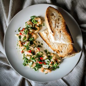 Top view of shrimp with herbs and toasted bread on a white plate.
